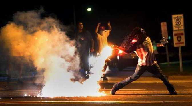 Black man wearing us flag shirt throwing tear gas cannister back at police in Ferguson MO USA